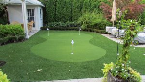 a lazy 8 shaped artificial golf green surrounded with landscape grass by swimming pool