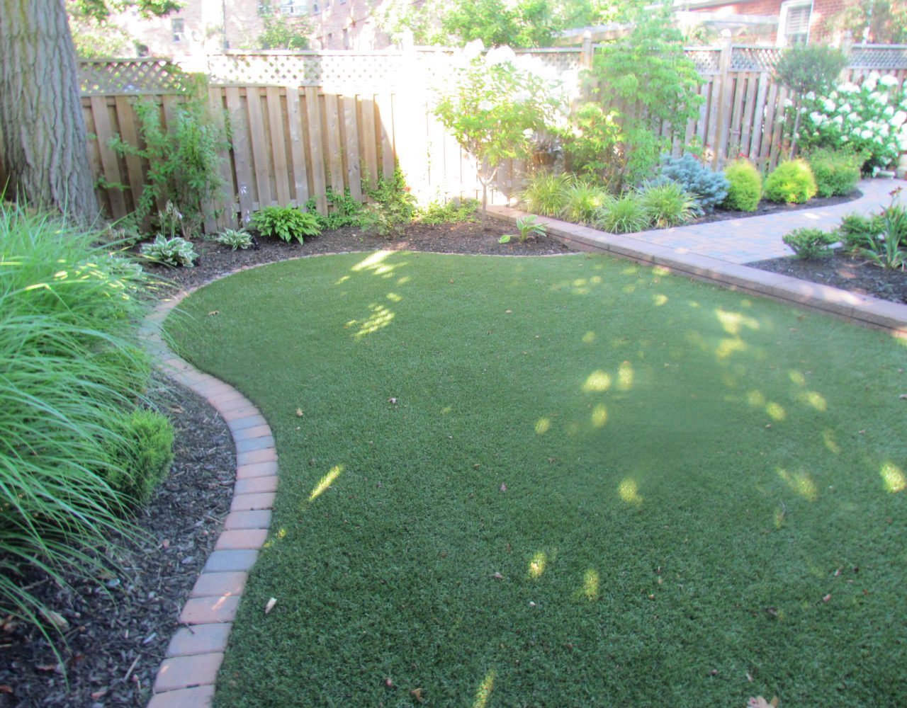 Synthetic lawn surface framed with Unilock pavers creates separation from garden